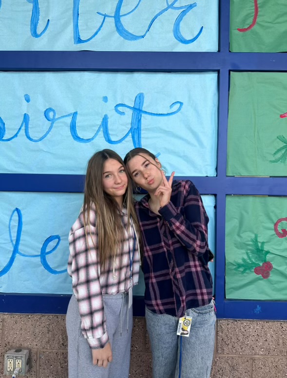 Feeling festive with their flannel-fueled spirit, Sloan Mcguire (9) and Piper Watson (9) pose together in front of the winter week poster.