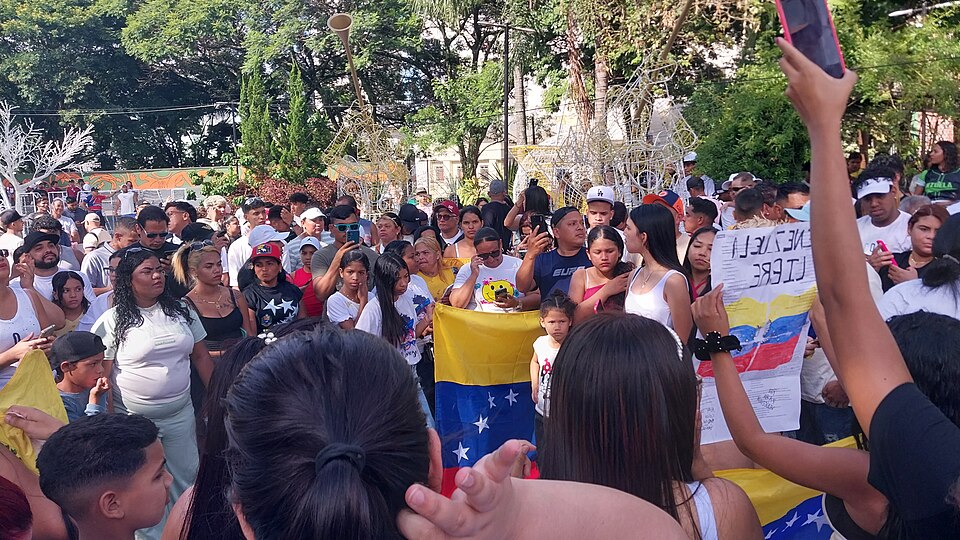 Venezuelans in Brazil celebrate following the U.S.-led attack on Venezuela and the capture of Maduro. (uploaded to Wikipedia by user KittyTeggie under CC-by-SA 4.0, https://commons.wikimedia.org/wiki/File:Venezuelans_celebrating_the_2026_United_States_strikes_in_Venezuela_in_the_Central_Plaza_of_Chapec%C3%B3,_Brazil.jpg)